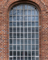 Brick building features large arched window with grid pattern and reflective surface in urban setting