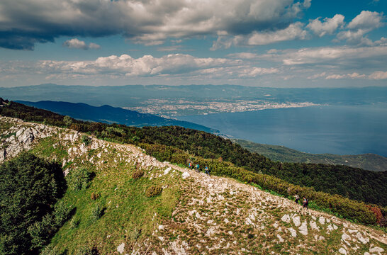 Aerial view of a rugged mountain ridge, where the green slopes meet the clear blue sea under a sky dotted with clouds, Mala Ucka, Primorje-Gorski Kotar County, Croatia.