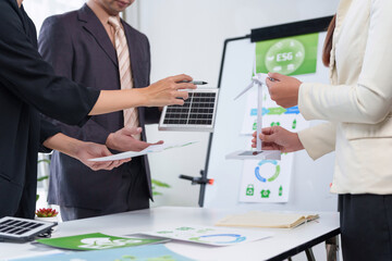 Business professionals discussing ESG strategy, holding solar panel and wind turbine models, focusing on sustainable development and renewable energy