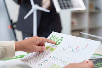 Person's hand pointing at an ESG report showing charts and data, with miniature wind turbine and solar panel in background