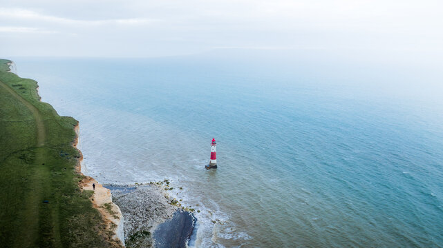 Aerial view of a striking red and white lighthouse standing steadfast against the crashing waves at the foot of the chalk cliffs, Eastbourne, United Kingdom.