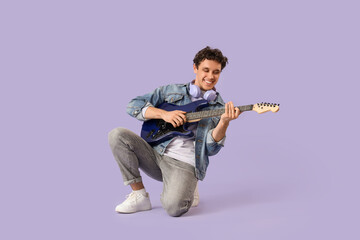 Young happy man with headphones playing new blue guitar on purple background