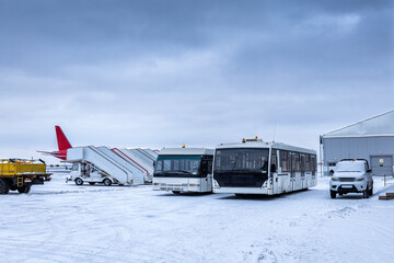 Two airport shuttle buses, empty passenger boarding stairs and other equipment on the winter airport