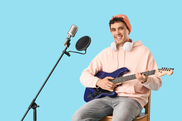 Obraz premium Young happy man with headphones and microphone playing new guitar against blue background