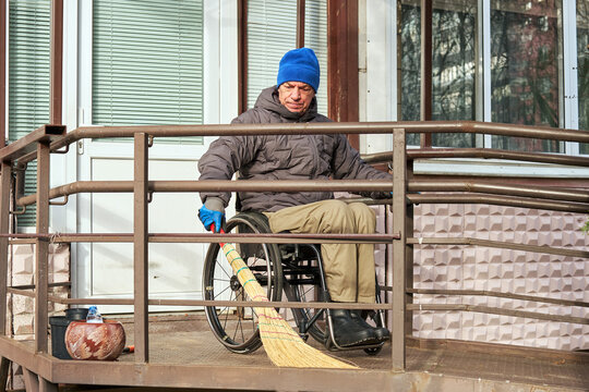A man in a wheelchair sweeps his ramp