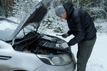 A man is repairing a car. A man is standing under the open hood of his car. A man is trying to start a car in freezing winter weather.
