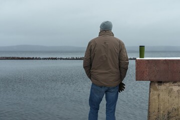 A man looks into the lake water. A young man stands by the lake and gazes into the distance. Outdoor recreation.