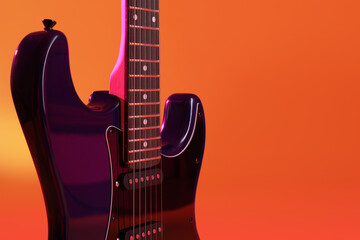 Modern electric guitar on orange background, closeup