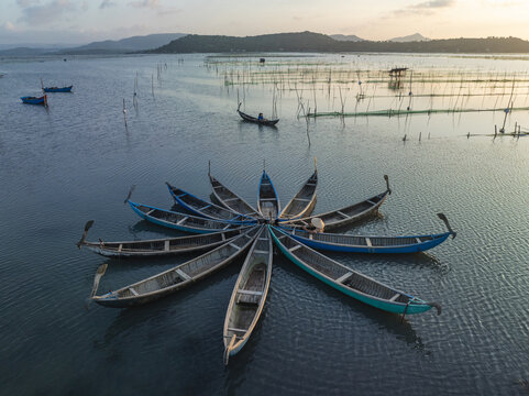 Aerial view of boats clustered in a star-like pattern on the water's surface, with distant fishing structures and a hazy horizon, Tuy An, Phu Yen, Vietnam