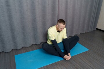 A young man is doing stretching exercises at home. Stretching and flexibility of muscles and joints. The man is working on his body's flexibility.
