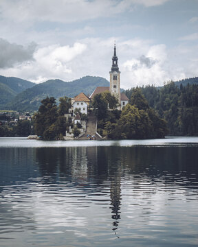View of the iconic island church mirroring in the calm waters of Lake Bled, surrounded by lush greenery and distant mountains, Bled, Radovljica, Slovenia.