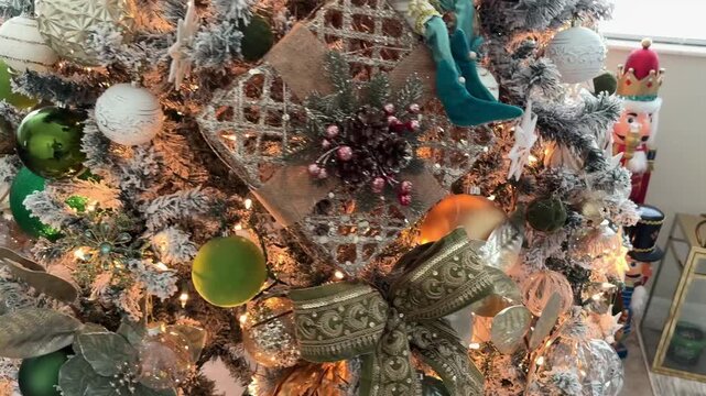 Close up of a decorated Christmas tree with a green ribbon bow, star ornaments, and mixed baubles in gold and white tones. Warm fairy lights create a cozy festive atmosphere at home.