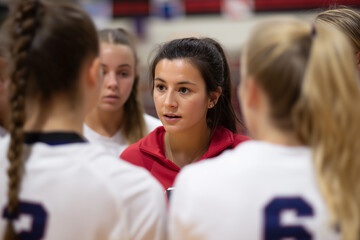 A focused volleyball coach engages passionately with her team in a huddle, inspiring motivation and teamwork during a crucial moment in a competitive match.
