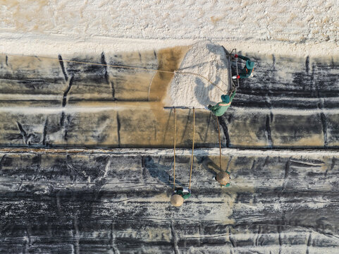 Aerial view of a worker carrying a heavy load of salt, contrasting starkly against the patterned salt fields, Phuoc Diem, Ninh Thuan, Vietnam.