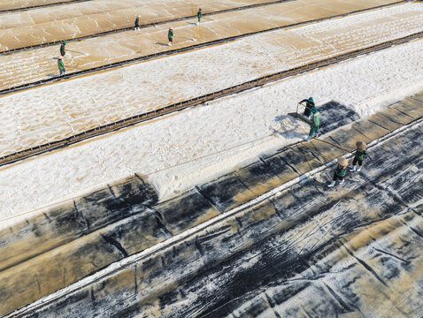 Aerial view of contrasting salt fields with workers harvesting under the sun, a mosaic of textures and tones unfolds, Phuoc Diem, Ninh Thuan, Vietnam.