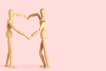 Wooden mannequins making heart gesture on pink background