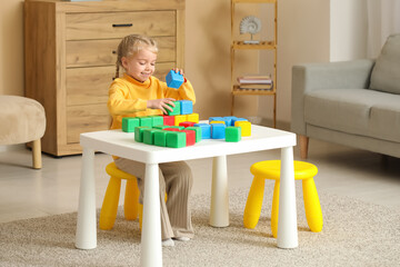 Cute little girl playing with plastic cubes at table in children's room