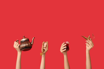 Female hands with Turkish tea, Aladdin lamp and prayer beads on red background
