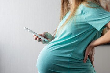 Fototapeta premium Pregnant woman using phone and holding her lower back in pain. 