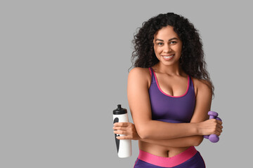 Naklejka premium Sporty young African-American female coach with water bottle and dumbbells on white background