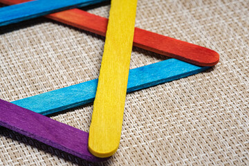Macro abstract photograph captures colorful craft sticks forming a conceptual geometric pattern on a textured background. Sticks are Suggesting an artistic, living metaphor. Use for creative design.