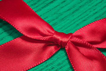 Extreme close-up detail of a vibrant red ribbon knot tied perfectly around a textured green surface. Symbolizing festive Christmas gifting and celebration. Ideal for holiday promotions.