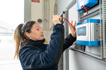 Female technician connecting electrical wires in control panel