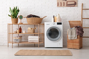 Modern washing machine, shelving unit, basket with laundry and ladder in room