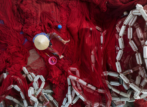 Aerial view of a person in a conical hat amidst a sea of vibrant red fishing nets contrasting with the stark white floats, Thuan An, B&igrave;nh Duong, Vietnam.