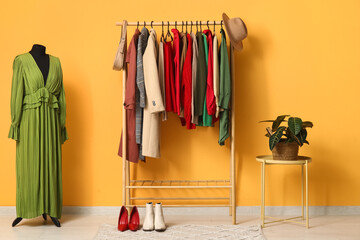Rack with clothes and mannequin near yellow wall in dressing room