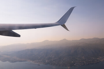 Fototapeta premium View of airplane wing over mountains and city landscape during sunset from high altitude