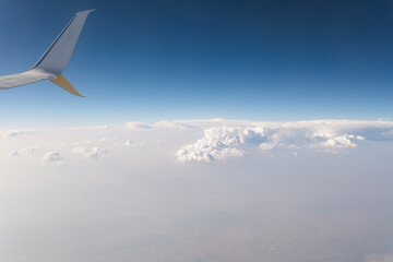 Obraz premium View from an airplane above the clouds during daylight with a clear sky and airplane wing present in the scene