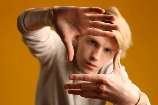 A handsome man framing a shot with his hands, looking at the camera against a yellow landscape. Studio shot.