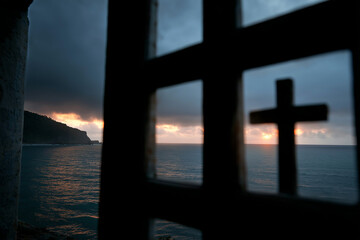 A tranquil seascape viewed through a cross-shaped frame, capturing the beauty of the ocean at sunset, symbolizing reflection and spiritual contemplation.