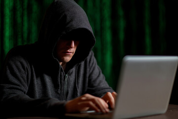 A shadowy figure cloaked in darkness works intently at a laptop, encapsulating an air of mystery and intrigue, which speaks to themes of secrecy and digital exploration.