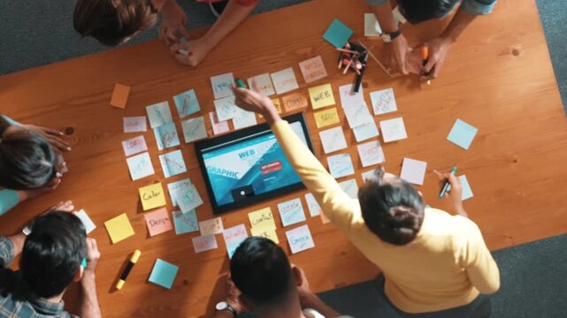 Top down view of programmer brainstorming and planning about web design while looking at tablet wireframe prototype. Aerial view of skilled developer team talking about digital application. Symposium.