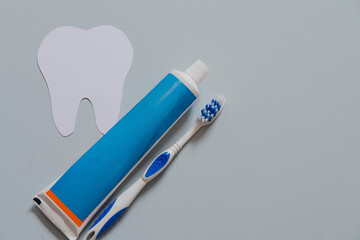Paper tooth next to toothpaste and toothbrush, copy space, blue background