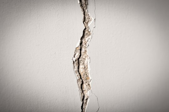 Macro view of a vertical cracked wall revealing damaged plaster and debris