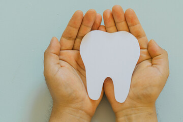 Hands holding a tooth figure, isolated light blue background