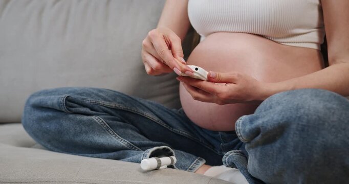 Pregnant woman sits on couch, holding fetal doppler device to monitor baby's heartbeat during pregnancy. Pregnant Woman Using Fetal Doppler