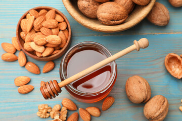 Honey in jar, nuts and dipper on light blue wooden table, flat lay