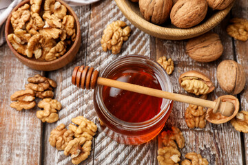 Honey in jar, walnuts and dipper on wooden table, above view