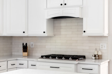 A kitchen detail with white cabinets and range hood, tan subway tile backsplash, and a stainless steel stovetop on a marble countertop.