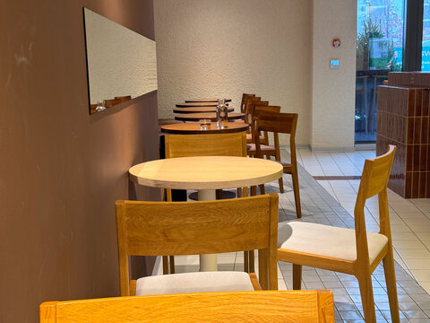 Minimalist cafe interior with empty wooden tables and chairs. Urban quietness, waiting, and everyday public space atmosphere during calm hours between social activity.