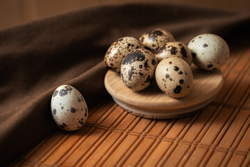 Quail eggs on a round wooden plate placed on a wooden surface with a brown linen napkin. Concept of natural nutrition, organic food
