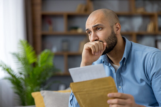 Young man reading important document, feeling stressed and anxious about an unexpected letter and current financial issues, representing debt, bankruptcy, and serious life challenges
