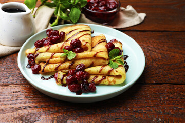Delicious crepes served with cherry jam and chocolate on wooden table, closeup
