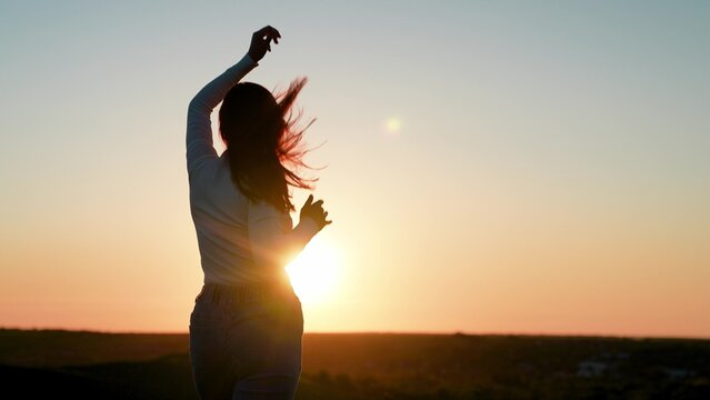 Young smiling woman dancing against sky outdoors. Holiday party. Beautiful girl dancing and having fun with friends at sunset disco. Cheerful woman moving her hands to music at party. Party on beach