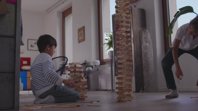 Boy stacking wooden blocks beside sibling&rsquo;s towering structure as both concentrate on shaping separate creations during focused creative play showing patience teamwork and calm determination indoors
