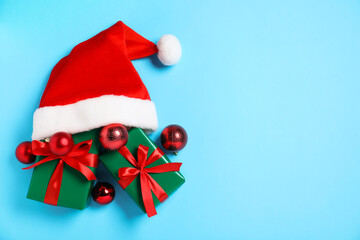 Santa hat, gift boxes and baubles on light blue background, flat lay with space for text. Merry Christmas and Happy New Year
